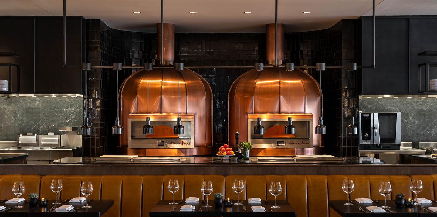 Restaurant interior, wine glasses on tables in front of a kitchen area